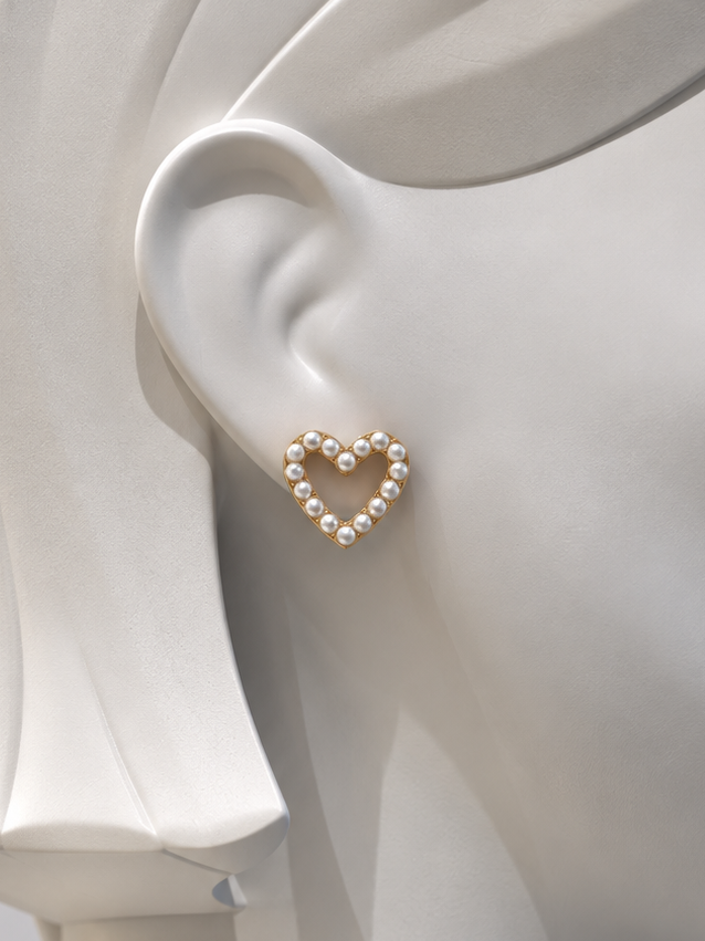 A gold heart-shaped stud earring adorned with small white pearls, shown on the ear of a white mannequin head.