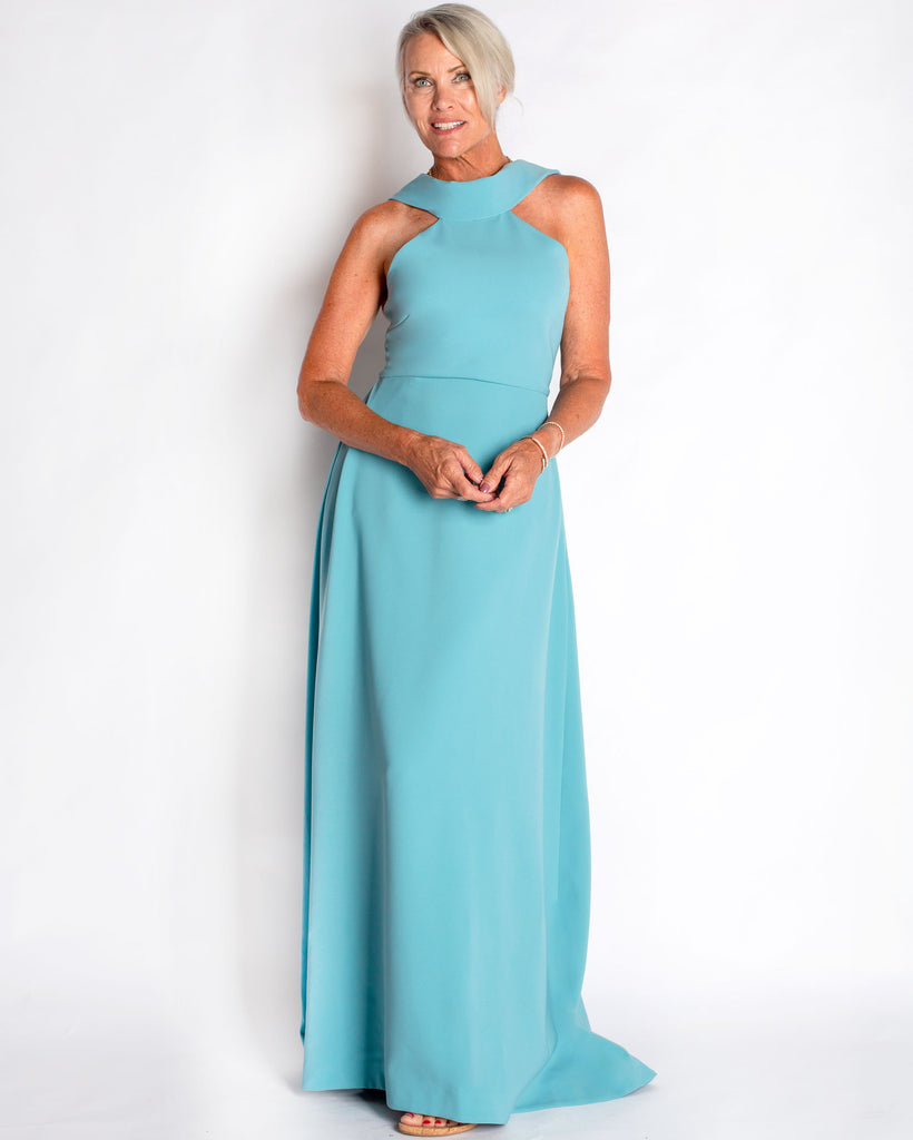 This floor length gown made in a stretch crepe material that is comfortable to wear. Fit & Flare silhouette flatters the bust through the waist and drapes over the hips. A halter bodice that has a rolled collar neckline with long tails that drape down the back in a loose tie. Made in a French Blue or Teal Color.